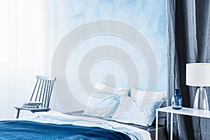 White lamp on table next to bed with navy blue bedding in bedroom interior with ombre wall