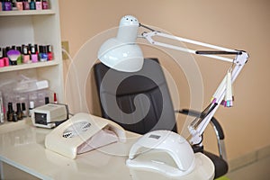 White lamp on white table with nail tool . Work place of nail amster with manicure tools, UV-LED lamp and nail polishes