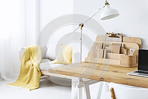 White lamp on wooden desk with laptop in bright freelancer`s interior with organizer.