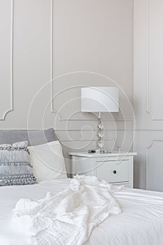 White lamp on wooden nightstand next to king size bed, copy space on grey empty wall