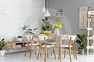 White lamps above wooden table and chairs in dining room interior with yellow flowers. Real photo