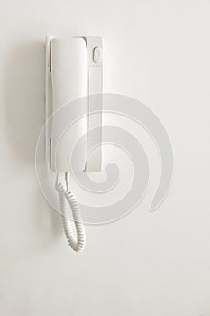 A white landline telephone is mounted on a white wall
