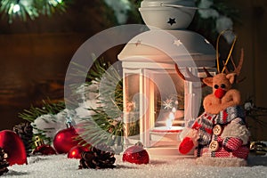 White lantern with a burning candle stands in the snow surrounded by Christmas decorations on the background of a wooden