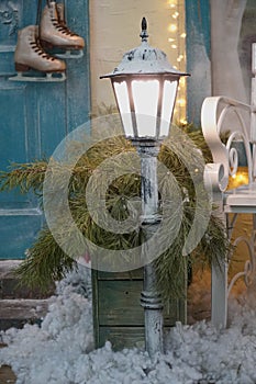 White lantern at the entrance to a private house in winter. skates hanging on the door handle, evergreen in a flower bed, strewn