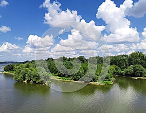 White large clouds over the river and trees.