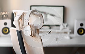 White large gaming headphones with a microphone hang on a white armchair. Close-up