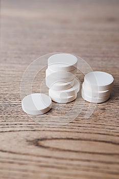 White large pills close up stand in a pile on a wooden background. Vitamins, pharmaceuticals for the treatment of diseases