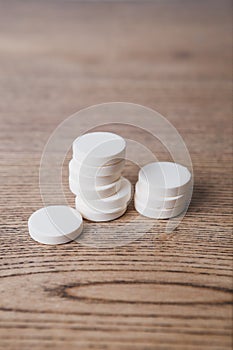 White large pills close up stand in a pile on a wooden background. Vitamins, pharmaceuticals for the treatment of diseases