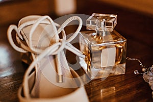 White leather shoe placed on a wooden table in front of a perfume bottle