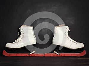 White leather skates for figure skating stand on a brown wooden background