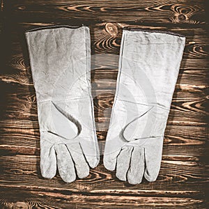 White leather welder gloves on a wooden background. A studio photo with hard lighting