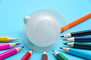 A white LED lamp surrounded by colored pencils on a blue background. The concept of one idea with a difference of opinion
