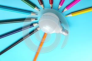 A white LED lamp surrounded by colored pencils on a blue background. The concept of one idea with a difference of opinion