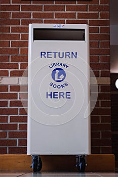 White library book return bin with the words Return Library Books Here on the front.