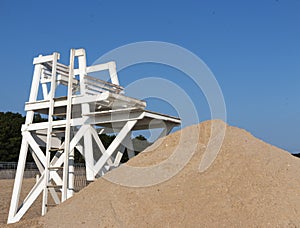 White lifeguard stand with sand pile in front and blue sky above