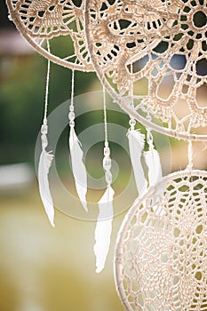 White light feathers hang on threads with transparent beads. Round dreamcatchers from macrame.