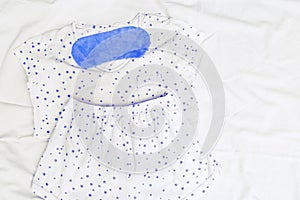 White Light pajama and blue eye mask on white sheet on bed. Night suit for peaceful sleeping