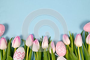 White and light pink tulip spring flowers and cute easter eggs in a row at bottom of light blue background with blank copy space