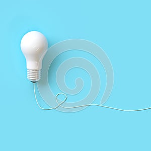 White lightbulb with wire on blue background for copyspace.