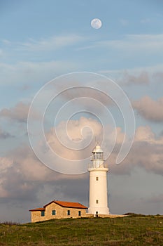 White lighthouse against the background of the evening sunset sky with clouds and a large moon. photo