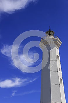 White lighthouse on a blue sky with white clouds.