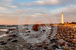 White lighthouse with red top at sunset near rocky sea.