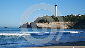 White lighthouse rises on a cliff, view from a sandy beach