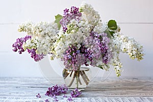 White lilac and purple lilac in glass vase on wooden table. Spring branches of blooming lilac festive bouquet of flowers