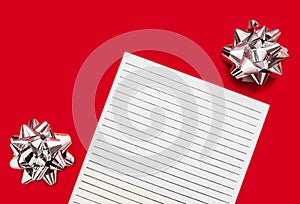 White lined sheet of paper on red background with a silver foil bow