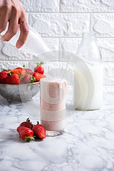 White liquid from a glass onto fresh strawberries in a small bowl