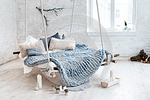White loft interior in classic scandinavian style. Hanging bed suspended from the ceiling. Cozy large folded gray plaid