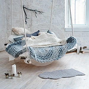 White loft interior in classic scandinavian style. Hanging bed suspended from the ceiling. Cozy large folded gray plaid