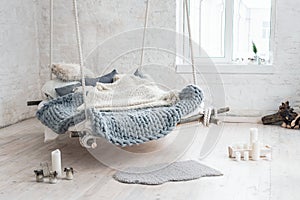 White loft interior in classic scandinavian style. Hanging bed suspended from the ceiling. Cozy large folded gray plaid