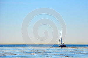A white lonely yacht is sailing along the shoreline