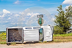 White long cab pick up truck turned on its side in a wreck at an intersection in the country beside a stop sign