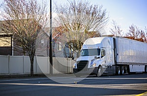 White long haul big rig semi truck transporting commercial cargo in dry van semi trailer running on the city street