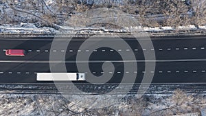 White Lorry truck with semi-trailer drives along black asphalt freeway: top view static drone shot.