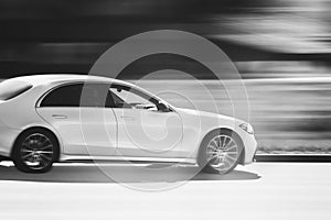 White luxury car is driving down the street at high speed. Abstract black and white photography of a fast moving blurred, white