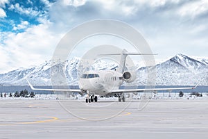 White luxury executive aircraft taxiing on airport taxiway in winter on the background of high scenic snow capped mountains