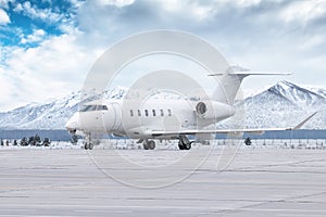 White luxury executive airplane taxiing on airport taxiway in winter on the background of high picturesque snow capped mountains