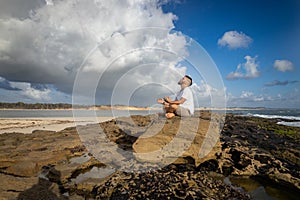 White man between 25 and 30 years old at the edge of the sea doing yoga