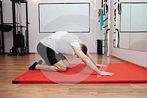 A white man is doing spine stretches on a red mat in the gym