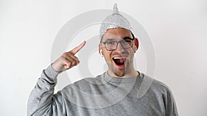 White man in a foil hat smiles and joyfully points his fingers at the tinfoil hat. 5G tower radiation protection.