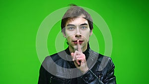 White man in leather jacket holding finger on his lips over green screen background.