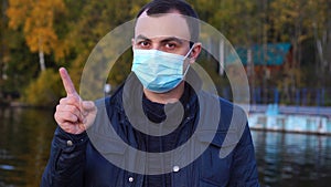 White man in medical protective mask disapproving with no finger sign make negation gesture.