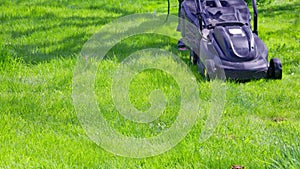 white man in plastic slippers moving green lawn with cheap plastic electrical lawn mover at sunny day, closeup