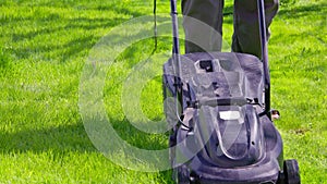 white man in plastic slippers moving green lawn with cheap plastic electrical lawn mover at sunny day, closeup