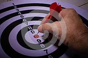 White man's hand placing a red dart in the center of black and white target. Selective focus