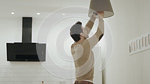 White man unscrewing light bulb at open kitchen. Guy standing under chandelier