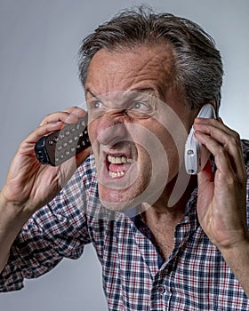 A white man yells while holding two cordless phones, with an expression of great stress